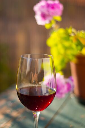 Glass of red wine on an old, rustic wood table. Enjoying it in the own garden in the evening sun.の写真素材
