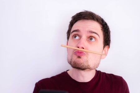Young Caucasian man is fooling around and home, pencil trapped between nose and lips