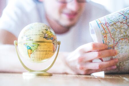 Miniature globe model and a young man looking in a map. Prepare for travelling. 