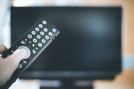 TV remote control in the foreground, tv in the blurry background.