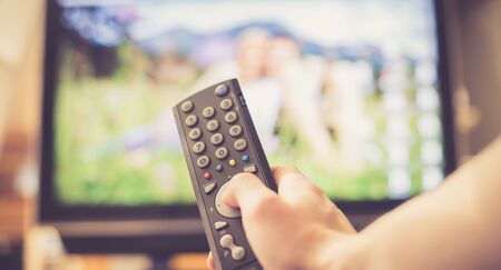 TV remote control in the foreground, tv in the blurry background. Film night with vod streaming.の写真素材