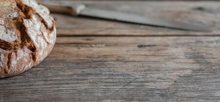 Fresh dark bread and knife on rustic cutting board, outdoors