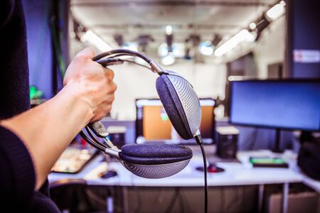 Young man holds headphones in the recording studio. Buttons, studio, screens and equipment in the blurry backgroundの写真素材