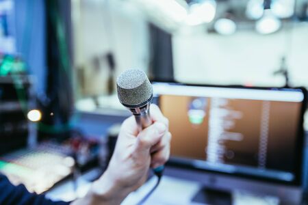 Young man is holidng a microphone in the recording studio, buttons and equipment in the blurry backgroundの写真素材