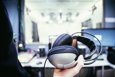 Young man holds headphones in the recording studio. Buttons, studio, screens and equipment in the blurry backgroundの写真素材