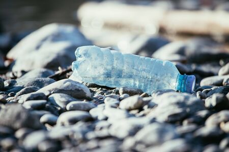 Plastic bottle is lying on the stony beach, environmental pollution