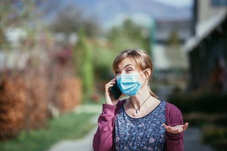 Young woman outdoors wearing a face mask and smartphone. Corona and flu season.の写真素材