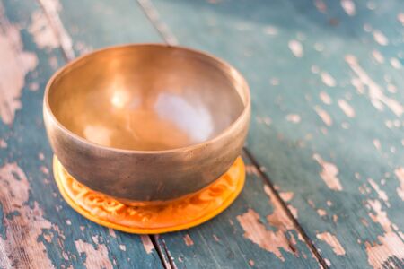 Metal singing bowl on a rustic green, wooden table outdoors. Flowers in the colourful, blurry backgroundの写真素材