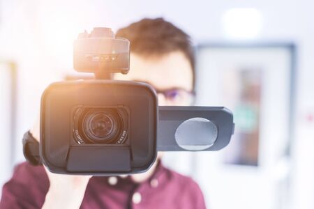 Male cameraman is holding a professional video camcorder, blurry backgroundの写真素材