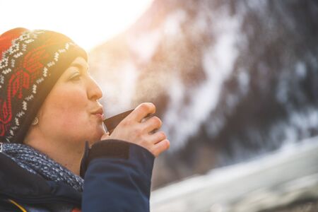 Beautiful Caucasian girl is holding a cup of tea outdoors, winter timeの写真素材