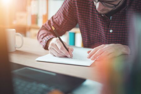 Young man writing on a white sheet, indoor at home officeの写真素材