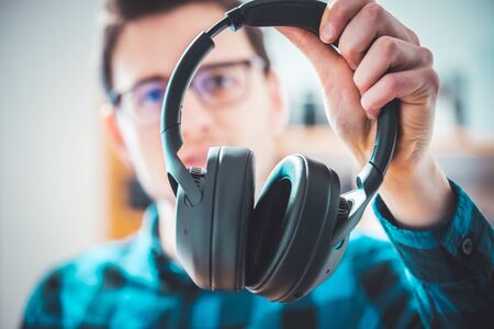 Young Caucasian man is holding black headphones, looking forward to listening to music.