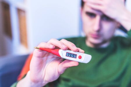 Man is holding a red fever thermometer in his handの写真素材