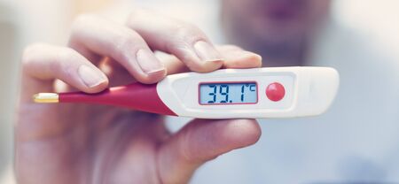 Man is holding a red fever thermometer in his hand