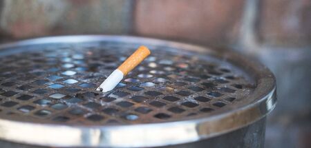 Closeup of cigarette in public ashtray. Extreme closeup, selective focus