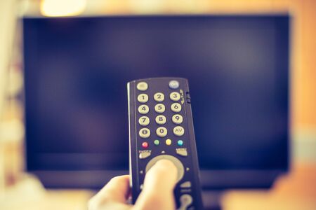 TV remote control in the foreground, tv in the blurry background.の写真素材