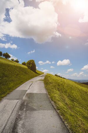 Idyllic mountain landscape, steep asphalted mountain road, green meadow and blue sky with cloudsの写真素材