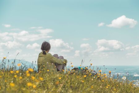 Sporty girl on a hiking trip is sitting on the meadow an enjoying the view over the far away cityの写真素材