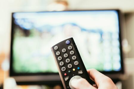 TV remote control in the foreground, tv in the blurry background. Film night with vod streaming.の写真素材