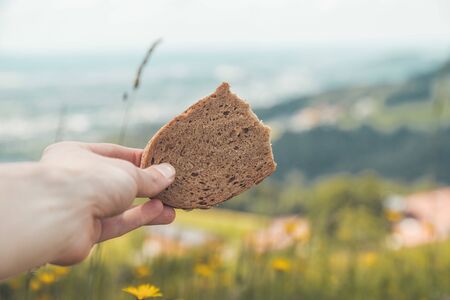 Piece of bread in male hand, idyllic landscape scenery in the defocused background