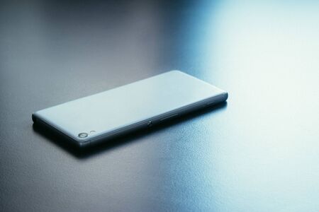 Modern white smart phone is lying on a grey surface or table, perspective viewの写真素材