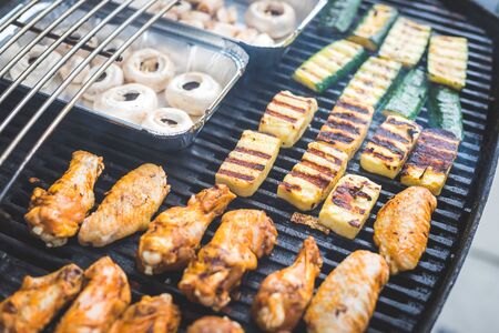 Close up of chicken wings, cheese and vegetables on gas grill. Summer time, outdoors.の写真素材