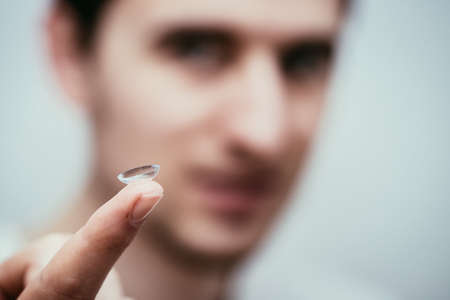 Close up picture of contact lens on a mans finger. Face in the blurry background.の写真素材