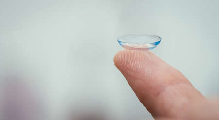 Close up picture of contact lens on a mans finger. Text space.