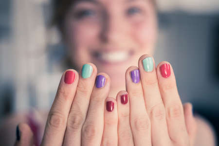 Close up picture of female fingers with colorful nail polish, face in the blurry background