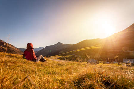 Woman in sportswear is enjoying the sunset in the mountains: sitting on the ground and enjoying the...