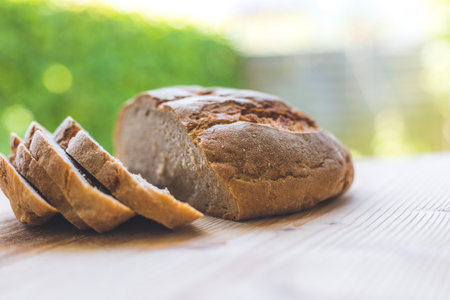 Fresh dark bread in slices, lying on a wooden cutting board. Defocused, blurry backgroundの写真素材