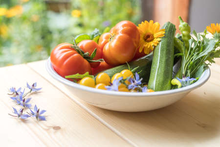 Fresh colorful vegetables in a bowl, raised in the own garden. Tomatoes, zucchini, flowers and herbs.の写真素材