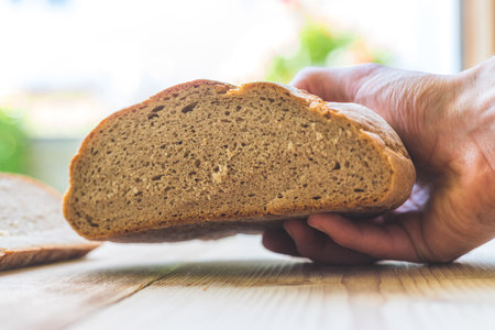 Male hand is holding a fresh rustic dark bread outdoors, breakfastの写真素材