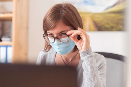 Young woman with glasses wearing face mask is working in the office during corona crisisの写真素材