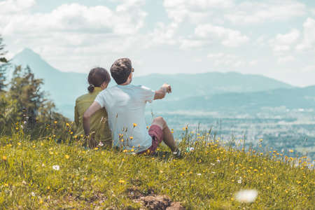 Couple on a hiking trip is sitting on the meadow an enjoying the view over the far away cityの写真素材