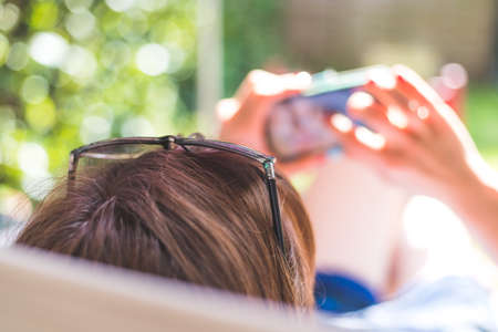Girl is sitting on the sunny porch, enjoying the day and using her smartphoneの写真素材