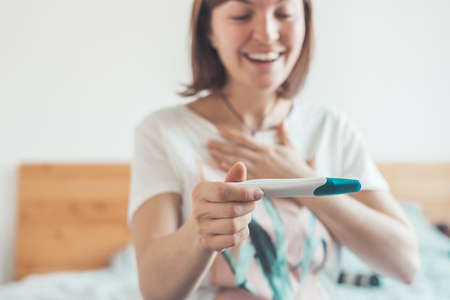 Happy mother holding pregnancy test in her hands, result is pregnant, "Schwanger"の写真素材
