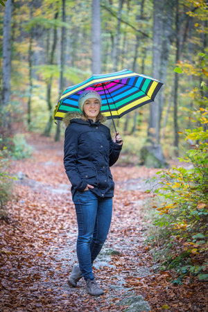 Young girl in blue coat and umbrella is taking a walk through the autumnal forestの写真素材