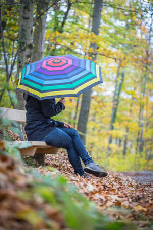 Young girl in blue coat and umbrella is taking a walk through the autumnal forestの写真素材
