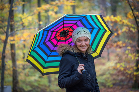 Young girl in blue coat and umbrella is taking a walk through the autumnal forestの写真素材