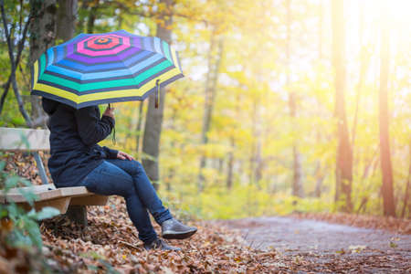 Young girl in blue coat and umbrella is taking a walk through the autumnal forestの写真素材