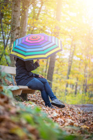 Young girl in blue coat and umbrella is taking a walk through the autumnal forestの写真素材