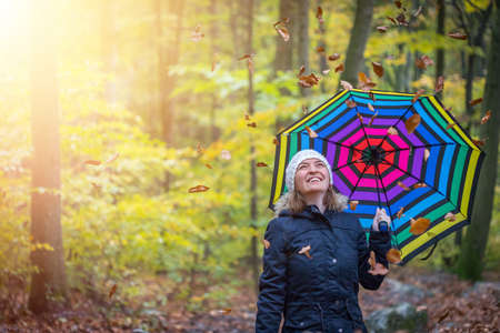 Young girl in blue coat and umbrella is taking a walk through the autumnal forestの写真素材