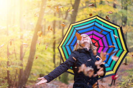 Close up of pretty young girl with a colorful umbrella in autumnal forest. Leaves are falling down.の写真素材
