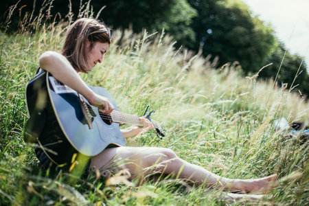 Beautiful young girl is sitting at a river and playing her western guitar