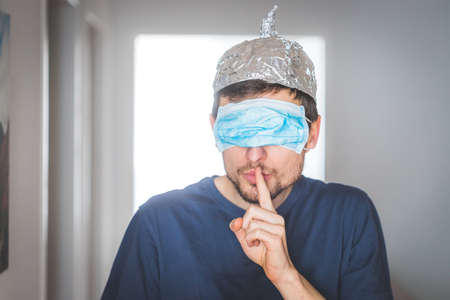 Young angry man with face mask over the eyes and aluminum hat is doing a psst! gestureの写真素材