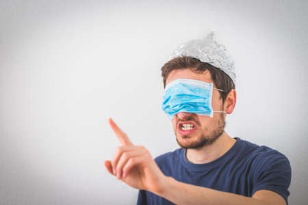 Young angry man with aluminum cap and face mask over the eyes is gesturing angry. Conspiracy theory concept.の写真素材