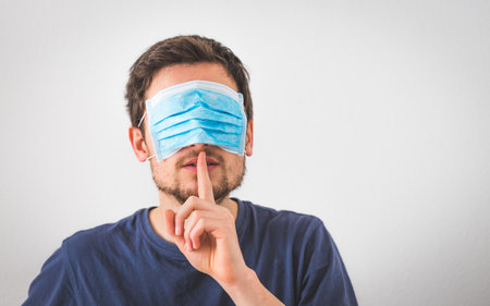 Young angry man with face mask over the eyes is doing a psst! gestureの写真素材