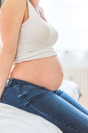 Caucasian pregnant mother touching her naked tummy, blue jeans, close upの写真素材