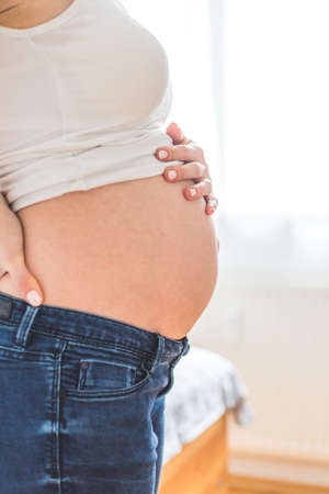 Caucasian pregnant mother touching her naked tummy, blue jeans, close upの写真素材